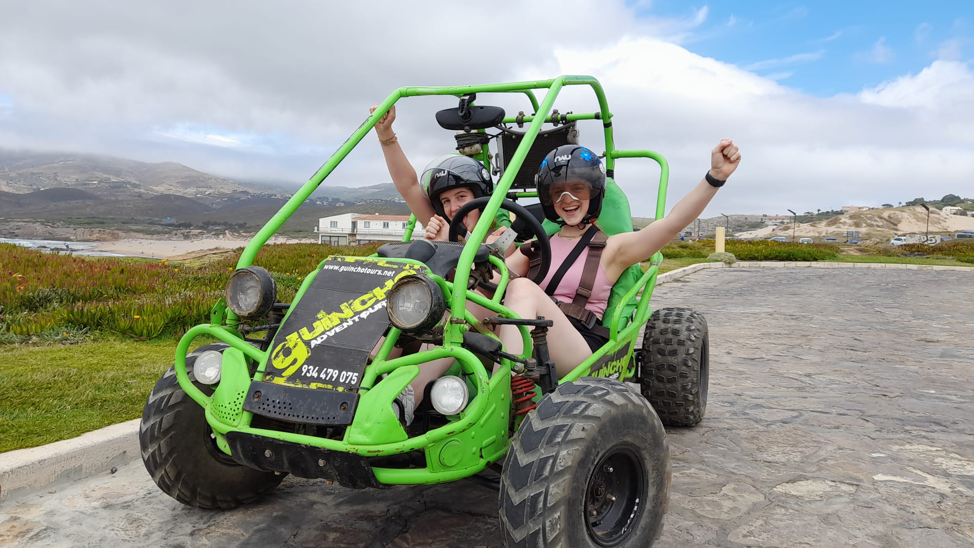 Two riders celebrating in a green Guincho Adventours buggy at the coast