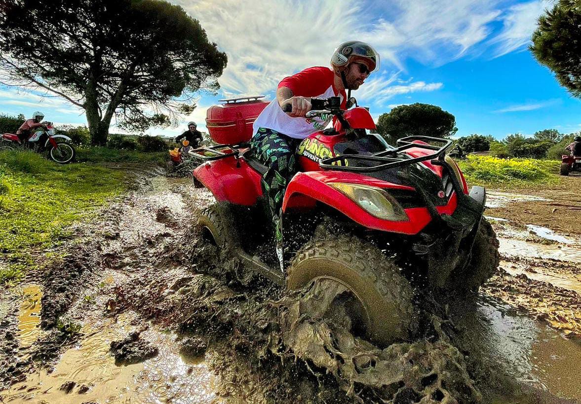 Rider splashing a red quad through mud on the Guincho trails
